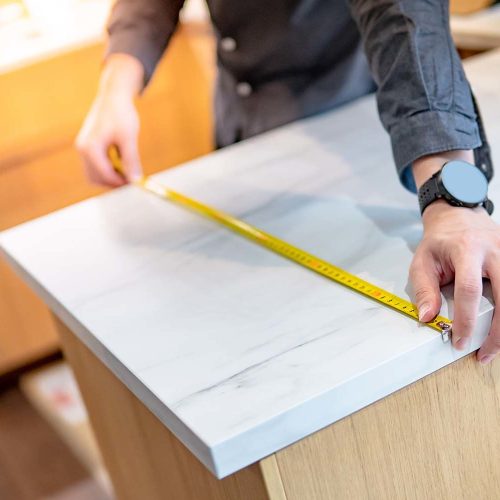 Male hand designer using tape measure for measuring white granite countertops on modern kitchen counter in showroom. Shopping furniture material for home improvement. Interior design concept